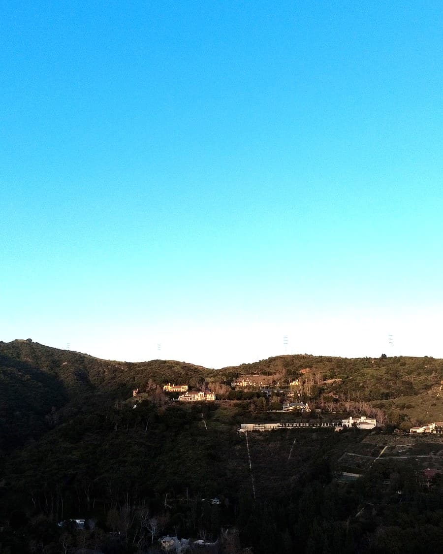 Wide aerial of a hillside community spread along a ridge at the edge of open wildland